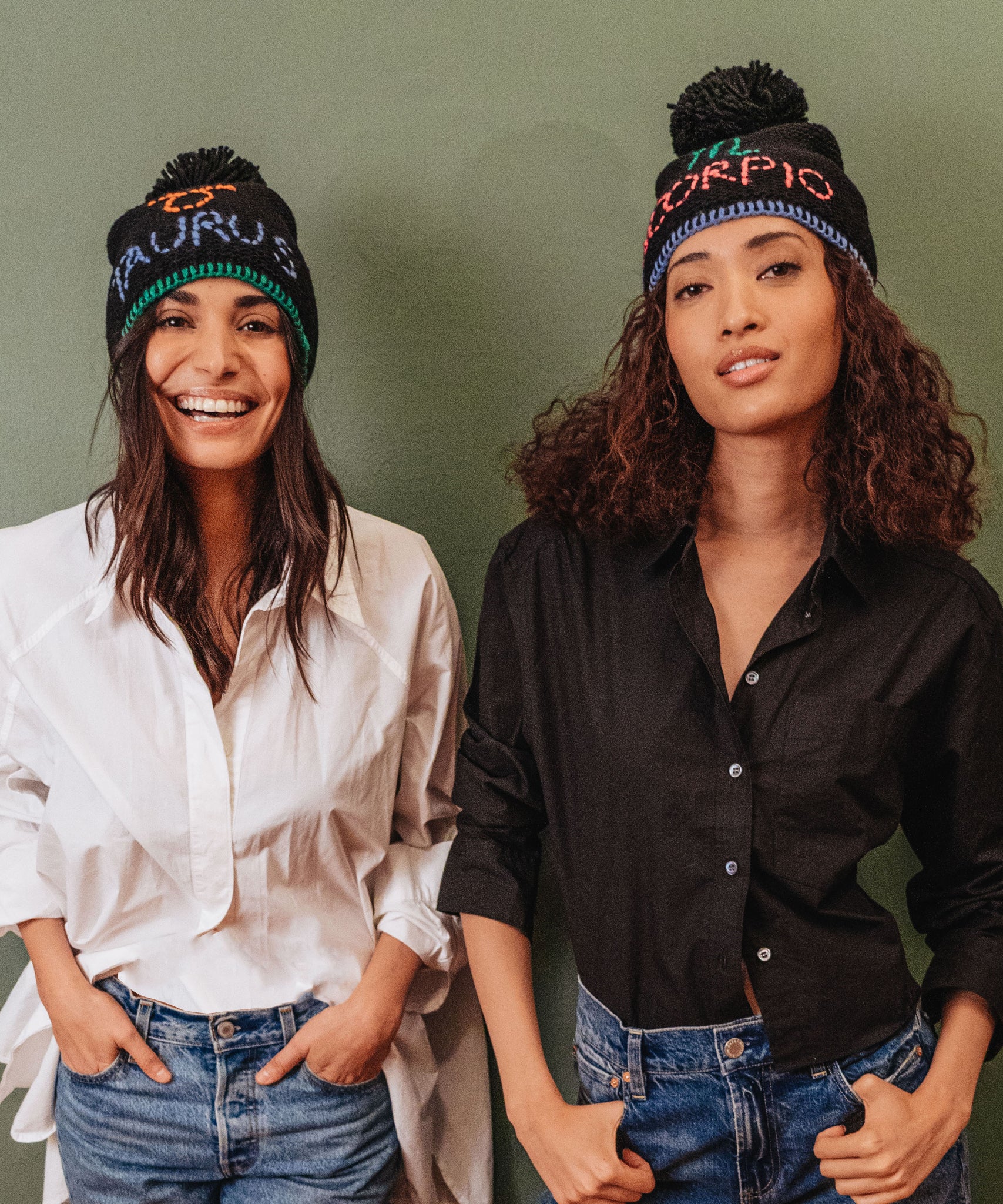 Two models in horoscope beanies.  One is Taurus and one is Scorpio.